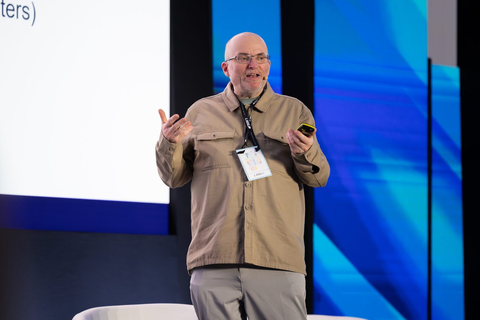 Dominik Lukeš speaking on stage at ISE 2025, mid-gesture with a slide clicker in his hand